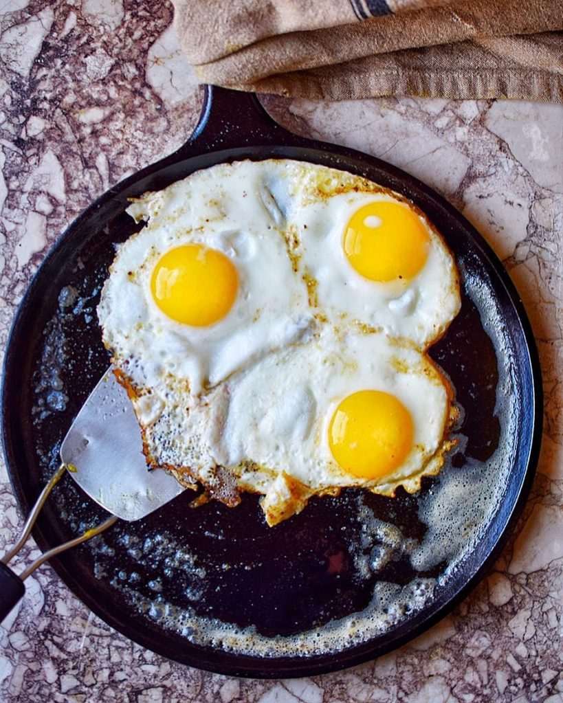 Cast iron skillet with fried eggs resting in soft morning light, the stove off and the kitchen quiet.